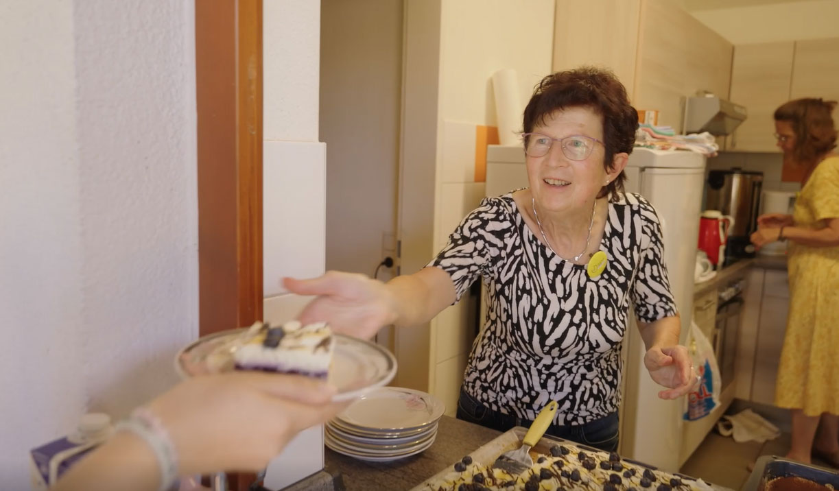 Frau reicht Kuchen an Gäste beim Kaffeeklatsch
